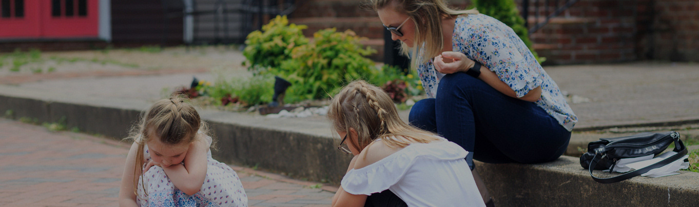 Photo of two children and their mother using chalk in a downtown street